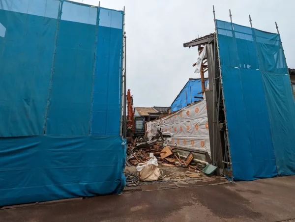富山の株式会社エイキ　ブルーシートで両脇を固める解体工事　重機による解体中