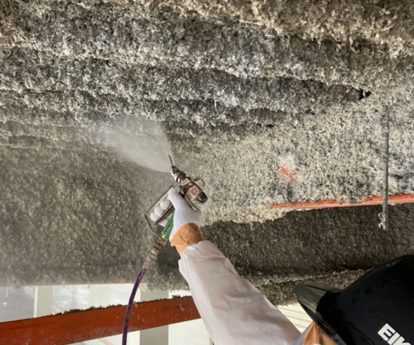 富山の株式会社エイキ(EIKI Inc.)の作業員が、吹き付けアスベストに飛散抑制剤を散布している様子