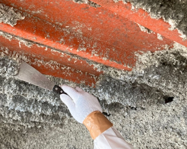 富山の株式会社エイキ(EIKI Inc.)の作業員が、ヘラで吹き付けアスベストを除去している様子