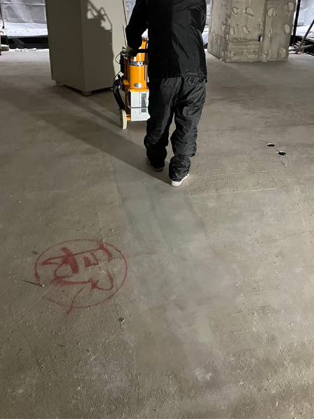 床研削機を手押ししている男性が床のアスベスト含有下地材を除去中