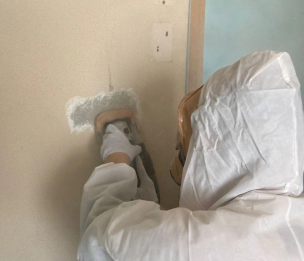 富山の株式会社エイキ(EIKI Inc.)が、壁の内壁塗膜材を除去している様子