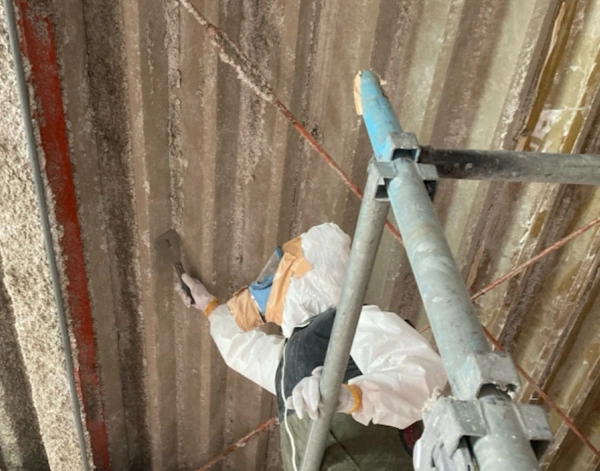 倉庫の天井の吹き付けアスベストを、ヘラで除去している様子
