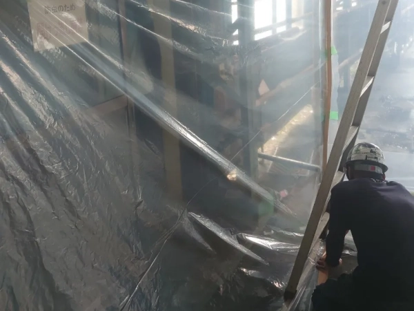 アスベスト除去現場の写真。外にアスベスト粉じんが漏れださないよう、株式会社エイキの作業員がシートを貼って養生作業を行っている。