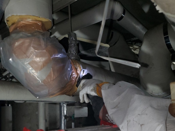 配管エルボにあるアスベスト保温材の除去作業風景。エルボのすぐ隣にレシプロソーの刃を入れて、切断している。