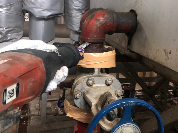 配管フランジにあるアスベストパッキンの除去作業風景。フランジのすぐ上にレシプロソーの刃を入れて、切断している。