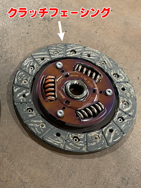 床に置かれたクラッチディスク。クラッチフェーシングを紹介する為、矢印で該当部分を記してある。