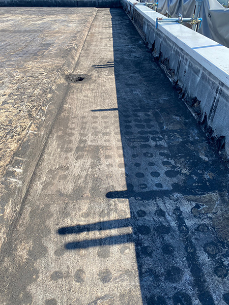 アスファルト防水材が除去されて下地材が現れた屋上。右にパラペットがある。