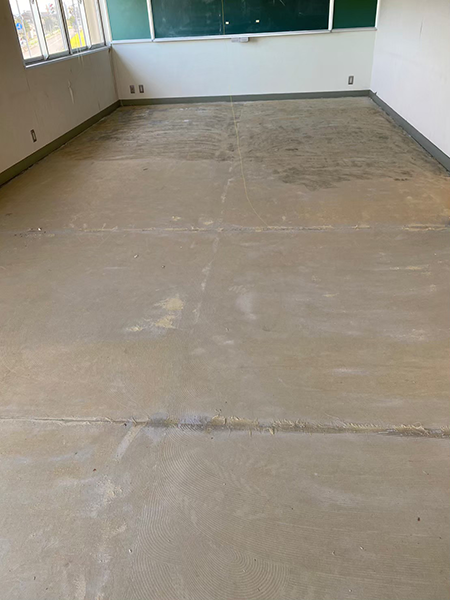 アスベスト含有長尺シートが剥がされて床の下地材のみの状態となった黒板のある部屋。