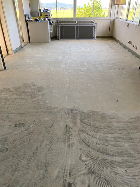 アスベスト含有長尺シートが剥がされて床の下地材のみの状態となった窓付きの部屋。