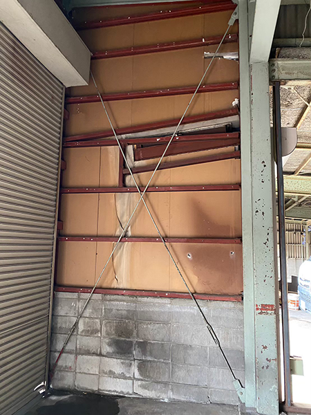 ケイカル板を外した倉庫の壁面。横の長さおよそ170cmの長細い鉄骨の躯体がおよそ60cmの間隔を開けて倉庫の天井まで縦に並んでいる。この躯体は右の太い鉄骨に取り付けられている。