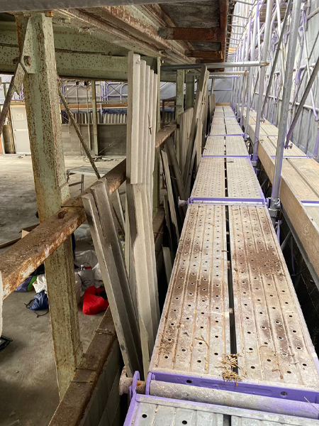 倉庫の背面の壁に足場を設置して波板スレートを取り外した様子。倉庫の内部が見える。