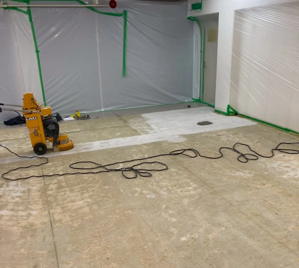 床の接着剤のアスベストを研削機で、削っている様子。周囲の壁には養生シートが貼ってある