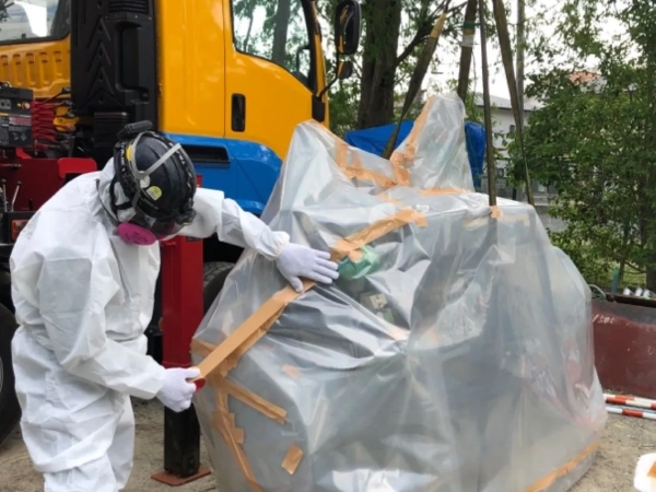 富山でポンプのアスベスト部品を除去。株式会社エイキの作業員がポンプをシートで包んでいる