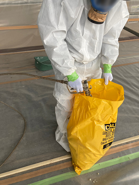 除去された吹き付けアスベストが入った廃棄袋へ、飛散抑制剤を散布して安定化させている作業員