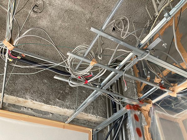 格子状の天井下地材と配線が絡み合っており、その更に上には天井スラブに吹き付けられたアスベストがある