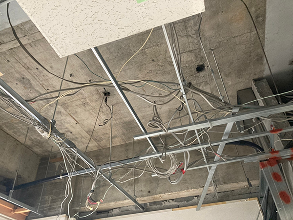 格子状の下地材と配線が絡まっており、その更に上の天井スラブは吹き付けアスベスト除去によって元のコンクリート同様の表面に戻っている。