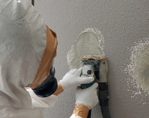 集塵機付きグラインダーを使用した外壁アスベストの削り取り作業をしている様子