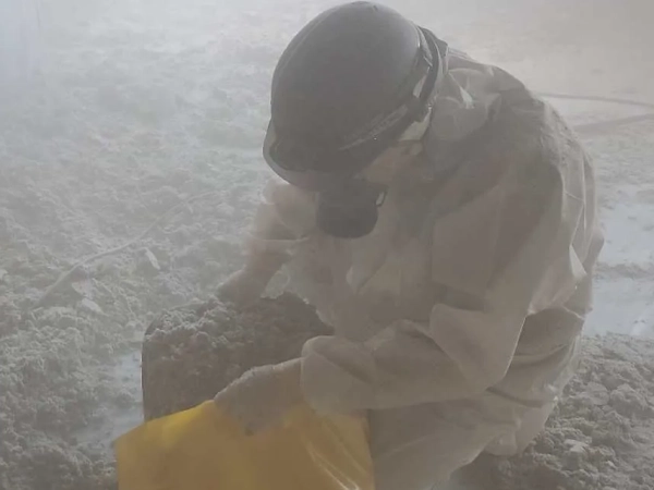 防塵マスクと防護服に身を包んだ株式会社エイキの従業員が、落としたアスベストを黄色の袋に詰めている。