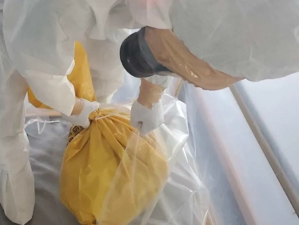 防塵マスクと防護服に身を包んだ株式会社エイキの従業員が、セキュリティゾーンの中で、アスベストが詰まった黄色の袋を二重梱包している。