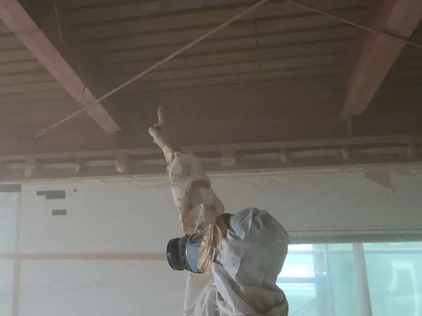 防塵マスクと防護服に身を包んだ株式会社エイキの従業員が、除去後の天井にアスベストが残っていないか指差し確認をしている。