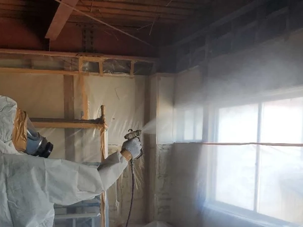 防塵マスクと防護服に身を包んだ株式会社エイキの従業員が、養生撤去前の安全対策として、再度飛散防止剤を散布している。