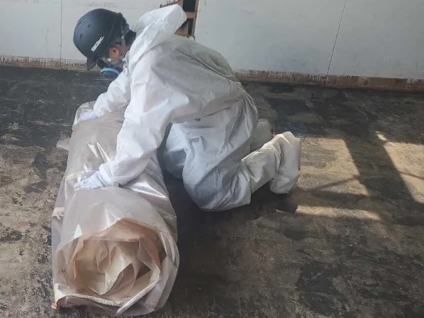 防塵マスクと防護服に身を包んだ株式会社エイキの従業員が、使用済み養生シートを包めている。