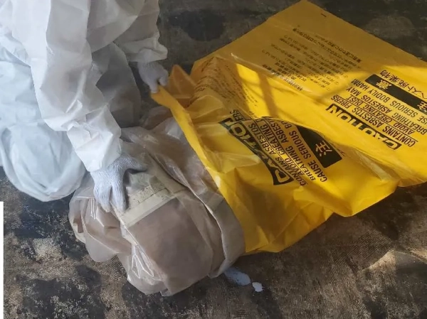 防護服を着た株式会社エイキの従業員が、使用済み養生シートを黄色の袋に詰めている。