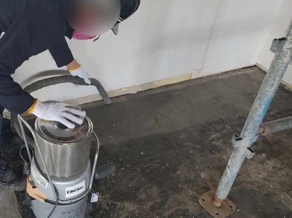 株式会社エイキの従業員が、エイキのロゴが入った真空掃除機で養生前現場を清掃中
