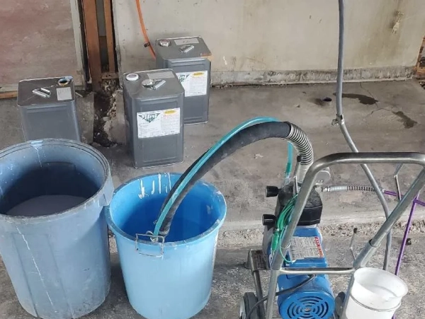 エアスプレー機を設置中の写真　奥にはアスベスト飛散防止剤の缶がある