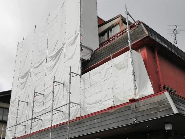 赤い外壁の3階建ての建物が防音シートで一部覆われている。