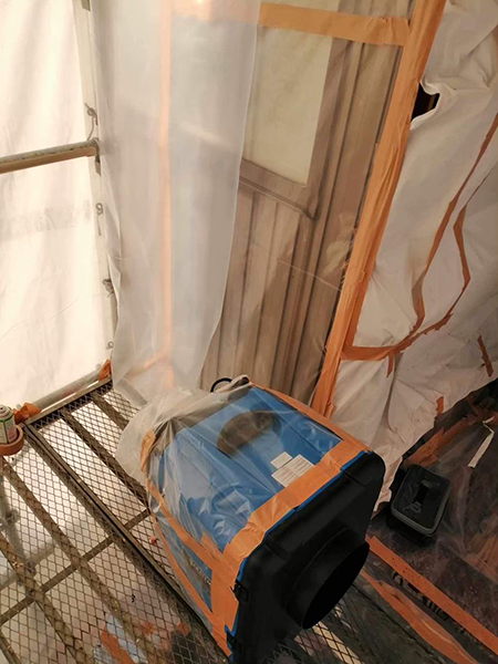 隔離養生内の足場の上に設置された負圧除じん装置。装置そのものも養生シートで覆われている