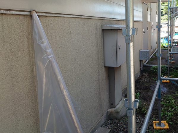 斜めから水平に写された、アスベスト塗材のある建物下半分の外壁。質感はざらざらしており、ボックス型の機械・ドアが取り付けられている。