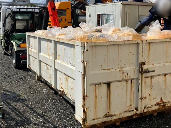 二重梱包された廃棄袋が外でトラックの荷台へ積まれている様子。