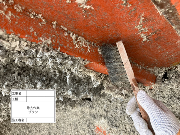 鉄骨に吹き付けられた吹き付けアスベストを、作業員がブラシでこすり落としている。