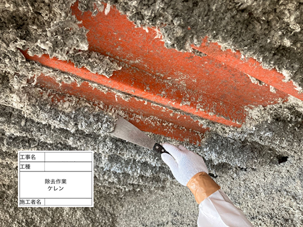 鉄骨に吹き付けられた吹き付けアスベストを、作業員がスクレーパーで削ぎ落としている。