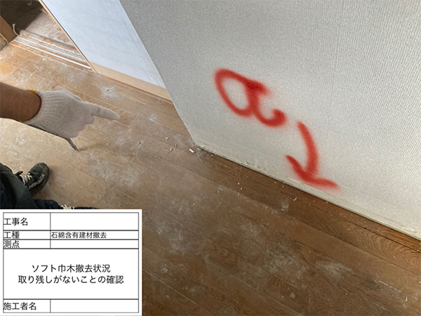作業員がアスベスト巾木を剥がした跡の壁に取り残しがないか、指差しで確認している様子。
