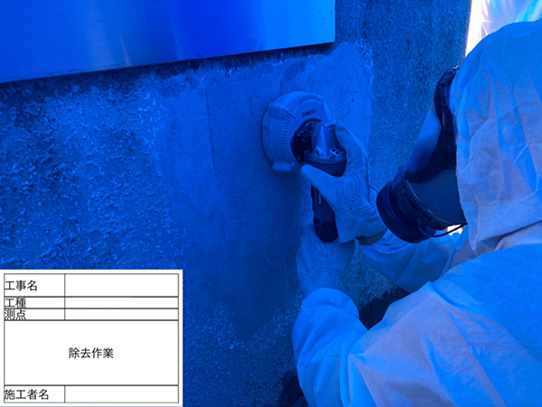 作業員が、コンクリート壁に集じん機付きディスクグラインダーで、アスベスト含有塗材を除去している様子。