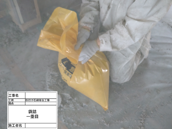 作業員が、吹き付けアスベストの入った袋を閉じて縛っている。