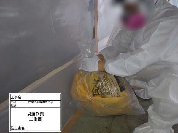 作業員が、吹き付けアスベストの入った袋をさらに透明な袋に入れて二重梱包している。
