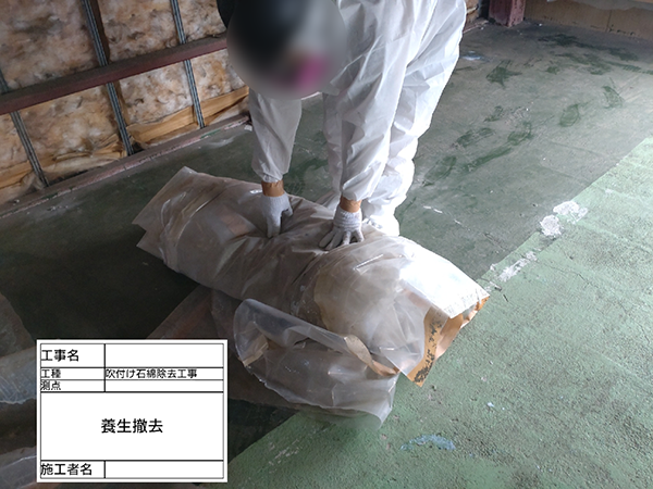 作業員が、剥がした養生シートを丸めている。
