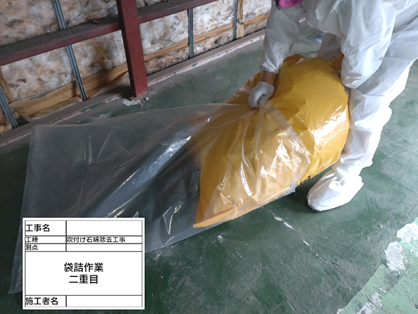 作業員が、丸めた養生シートを廃棄袋へ二重梱包している。
