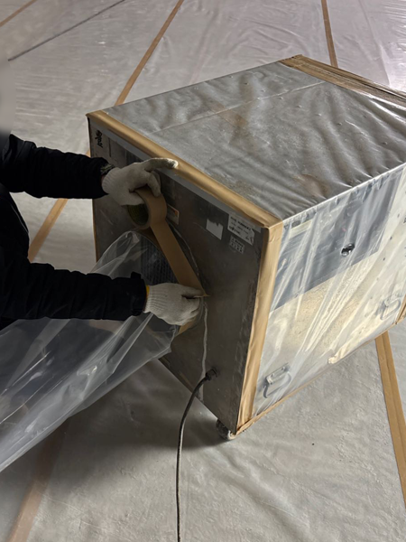 作業員が、負圧除じん装置の裏面の排気口に排気ダクトを接続し、テープを貼っている。