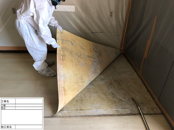 作業員が、ビニル床の端を両手で持って剥がしている。