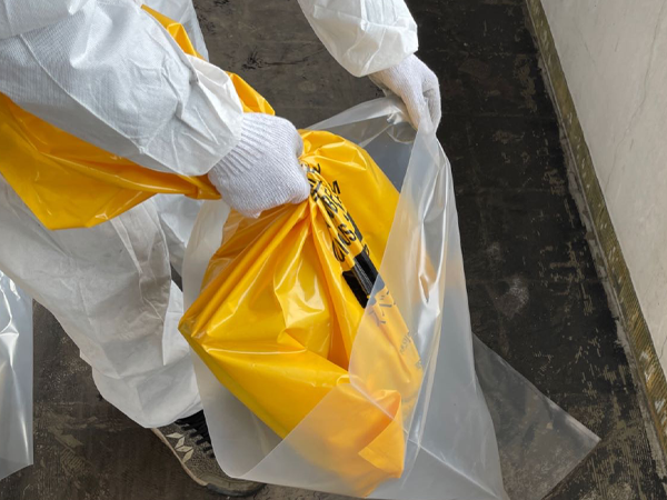 作業員が、配管エルボの入った廃棄袋を、透明な袋に入れている。