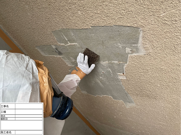 作業員が、タワシを使って天井に付着した細かな吹き付けバーミキュライトを除去している。