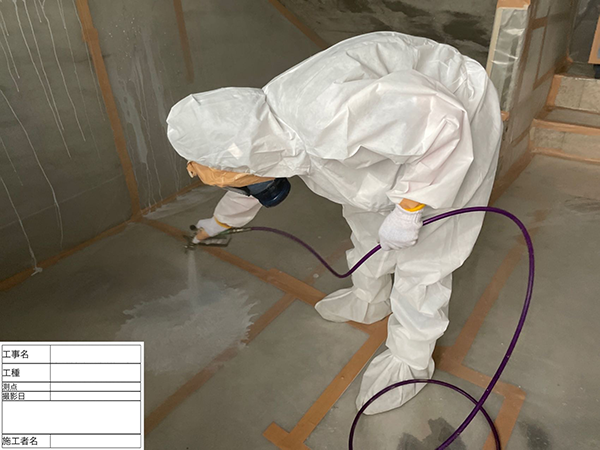 作業員が、除去作業後の養生シートにエアスプレーガンで飛散防止剤を散布している。