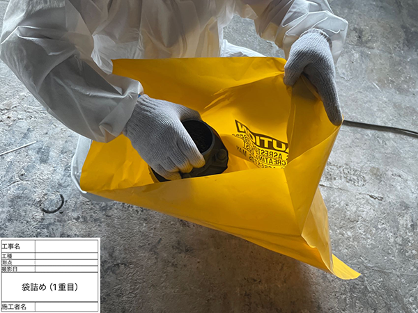作業員が、切断した配管フランジをアスベスト廃棄袋へ入れている。