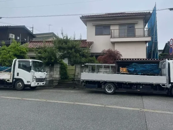 富山県内での解体工事現場の前の道路に、資材を積んだトラックが2台並んでいる写真