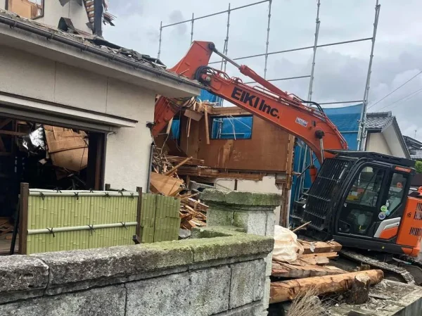 株式会社エイキのオレンジ色のユンボが建物を壊している最中の写真。