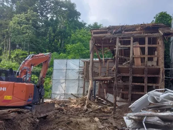 富山の土蔵解体現場。弊社のオレンジ色の重機が土蔵を外側から解体している写真。隣の地に廃材がおちないように、境目を養生しています。
